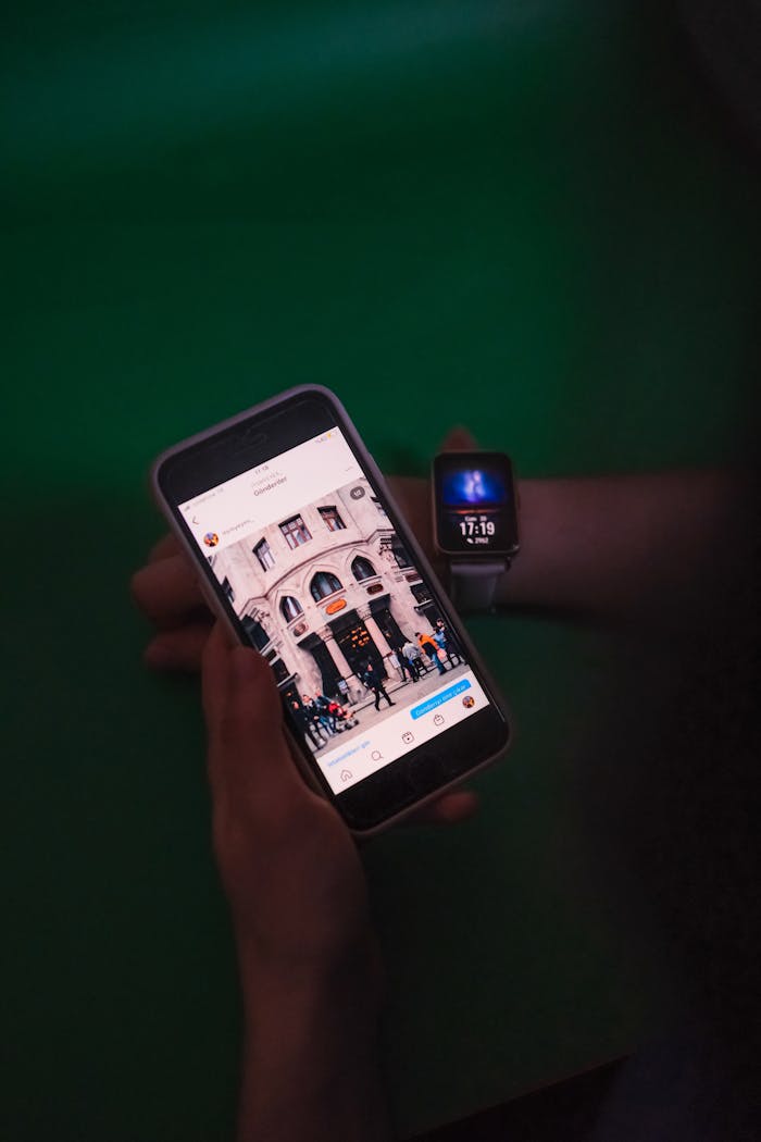 Close-up view of a person holding a smartphone displaying an image on Instagram, alongside a smartwatch against a green backdrop.