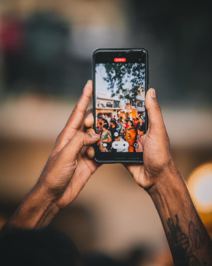 Hands holding a smartphone recording a colorful celebration in India, showcasing vibrant cultural festivities.